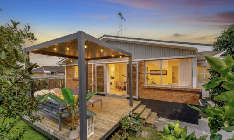 Brick and tile unit in Auckland with a timber deck and pergola at dusk