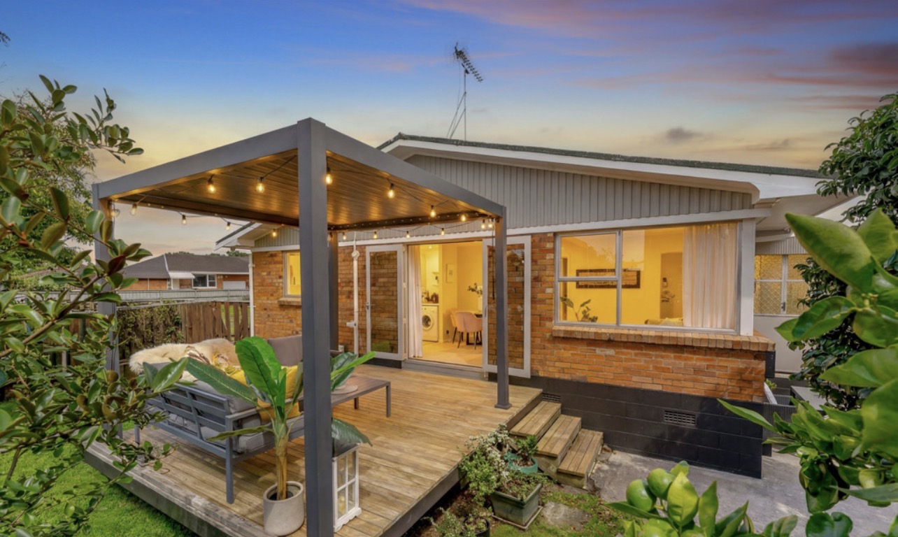 Brick and tile unit in Auckland with a timber deck and pergola at dusk